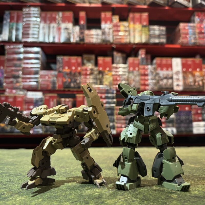 Tan and green 30 Minutes Missions robot models posed with rifles on a gaming table in front of hobby shop shelves.