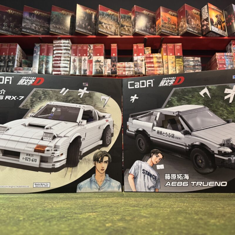 CaDA Initial D boxes showing Ryosuke’s white Mazda FC3S RX-7 and Takumi’s black-and-white Toyota AE86 Trueno side by side.