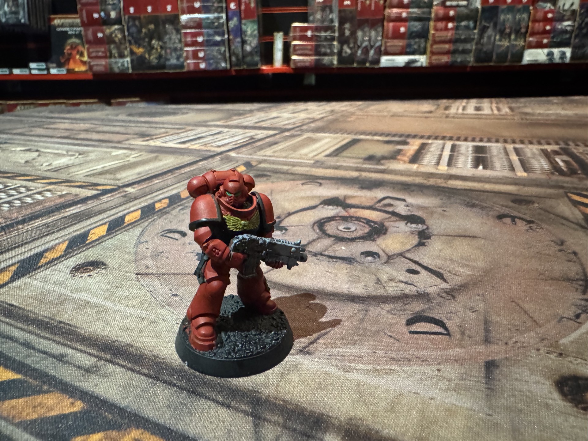 A painted Space Marine in red armour holding a bolter on a gaming table