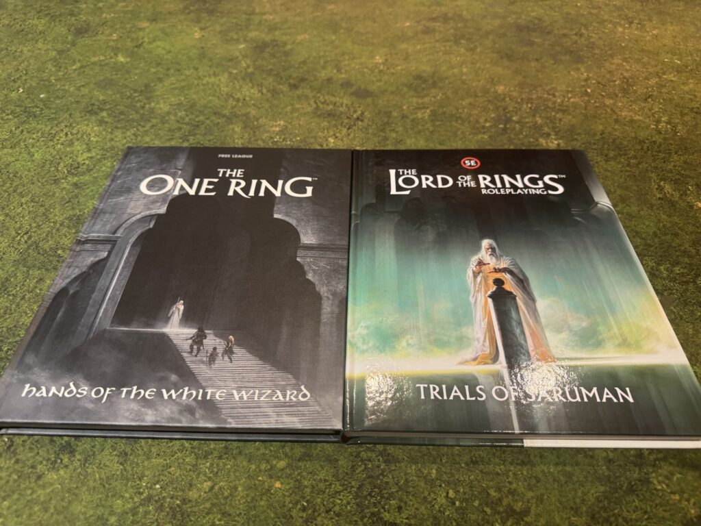 Hands of the White Wizard for The One Ring and Trials of Saruman for The Lord of the Rings Roleplaying 5E, side by side on a green gaming mat.