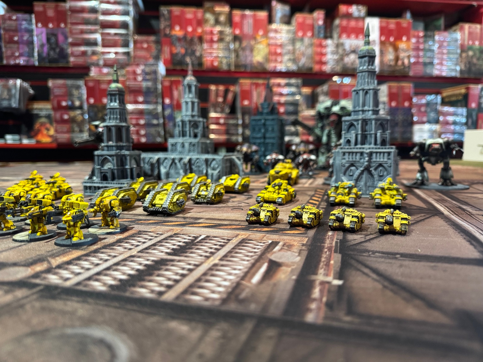 Yellow Legiones Astartes tanks and Dreadnoughts on a Legions Imperialis tabletop, with Titans and city terrain behind them.