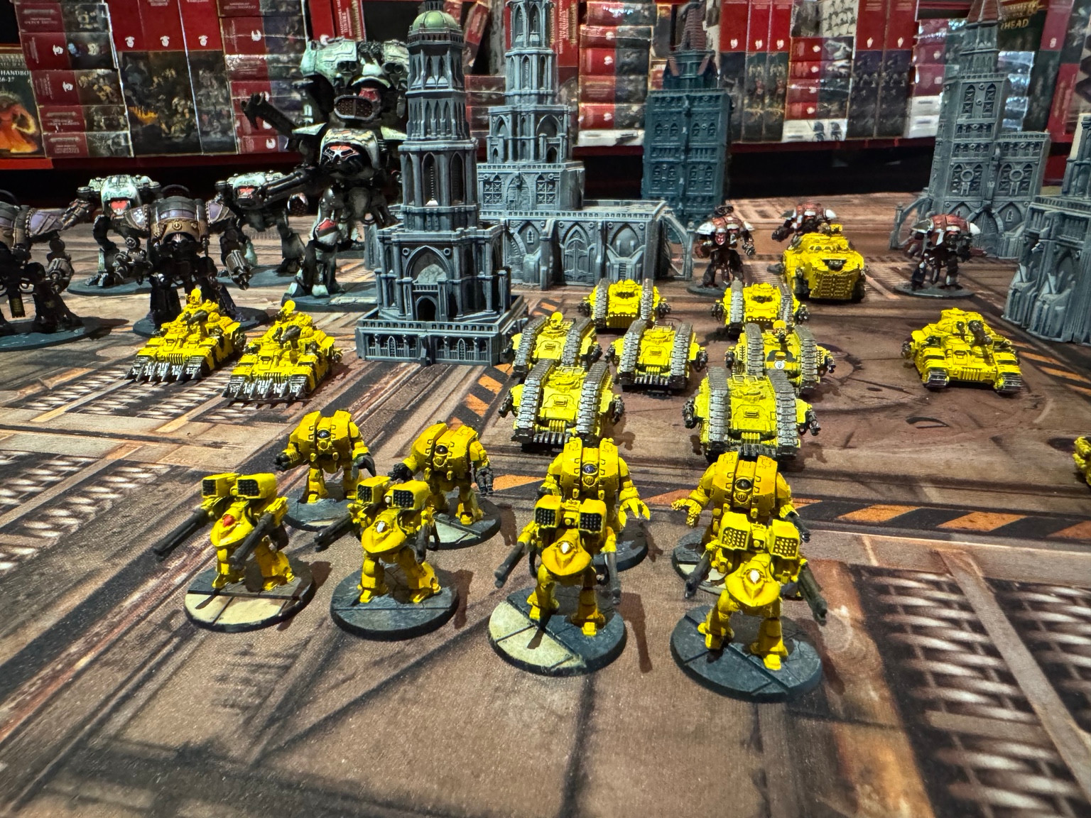 Yellow Legiones Astartes Dreadnoughts arranged in two rows, with armoured vehicles and city terrain behind them.